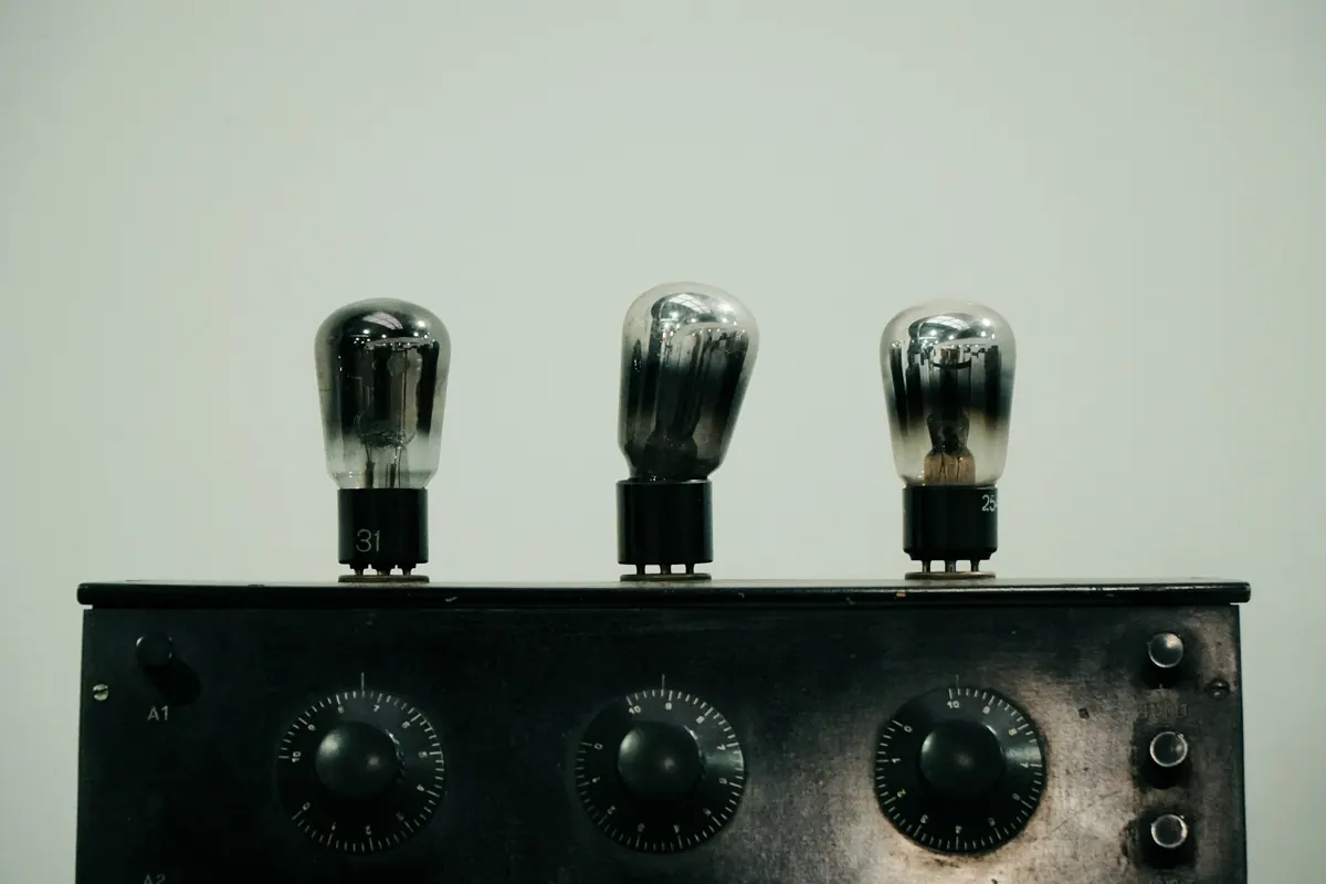 Three glass vacuum tubes standing on top of a vintage black chassis with three calibrated dials